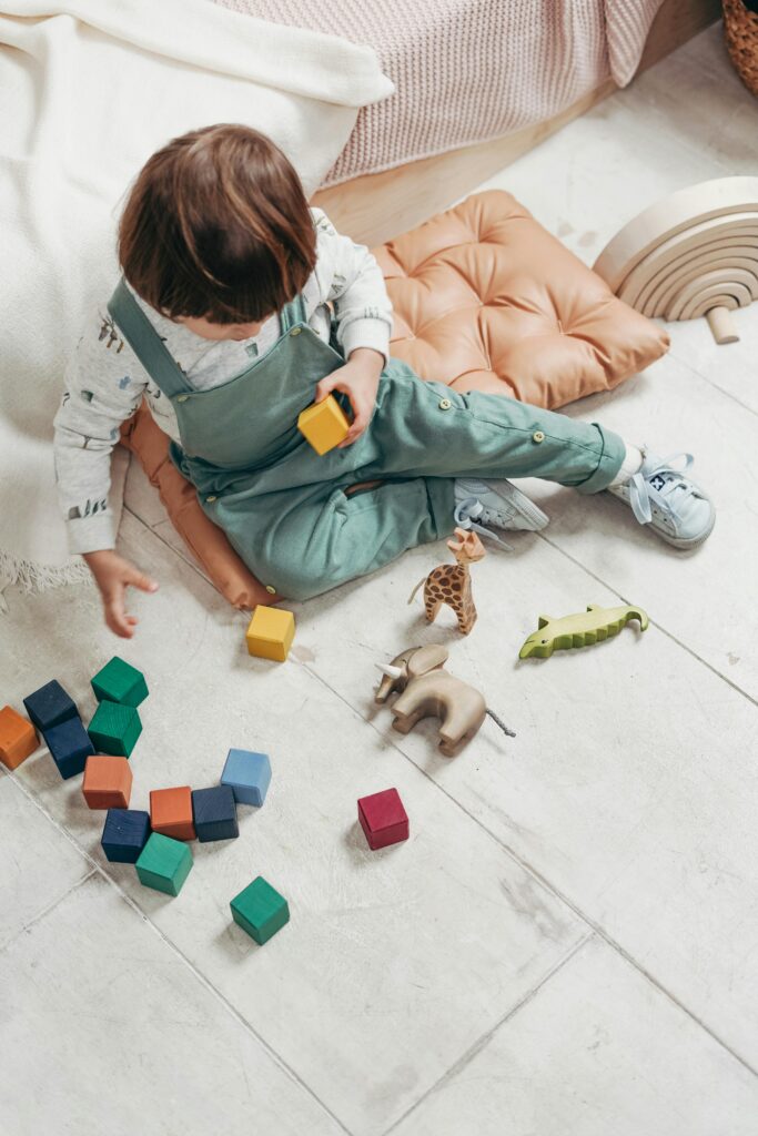 Un niño pequeño jugando con bloques de madera de colores y figuras de animales dentro de casa.