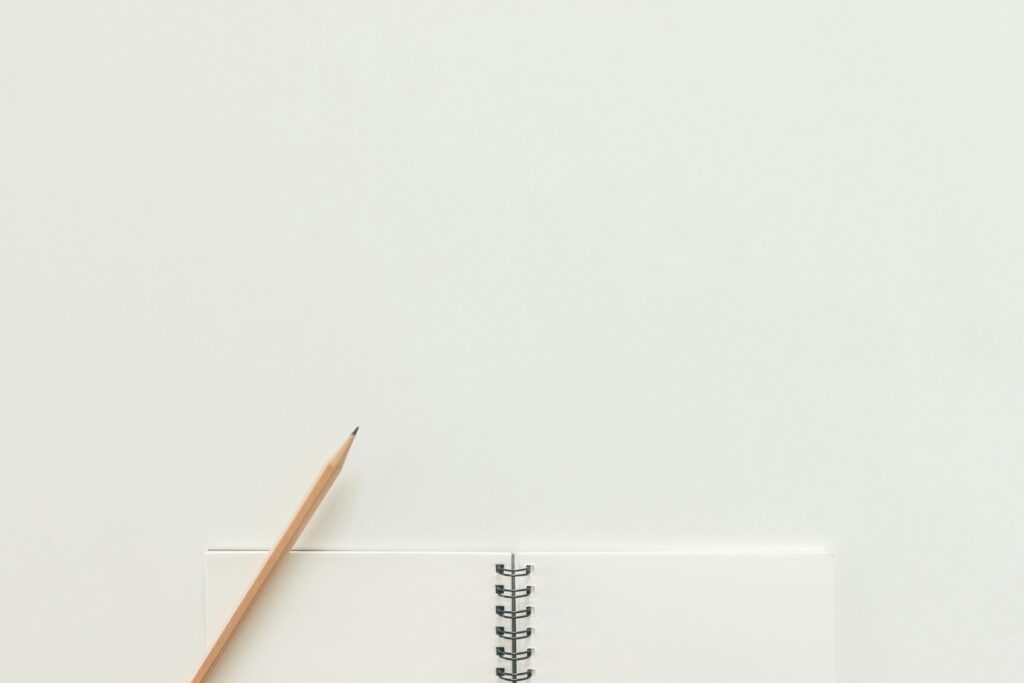 Vista superior de un cuaderno de espiral con lápiz sobre un fondo neutro claro, ideal para espacios de trabajo creativos.