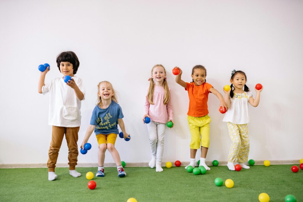 Diversos niños felices jugando con pelotas de colores en el interior, mostrando diversión y amistad.