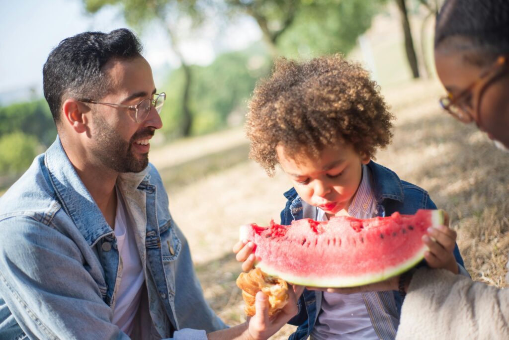 Padre e hijo comparten un momento de alegría durante un picnic, disfrutando de una sandía fresca al aire libre.