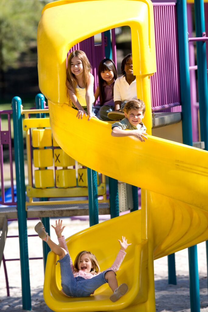 Children having fun on a colorful playground slide outdoors on a sunny day.