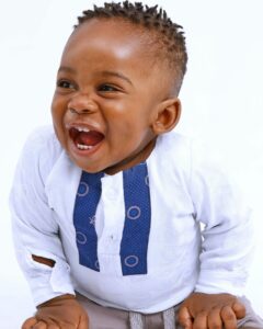 Adorable baby boy laughing joyfully in a white outfit, set against a clean white background.