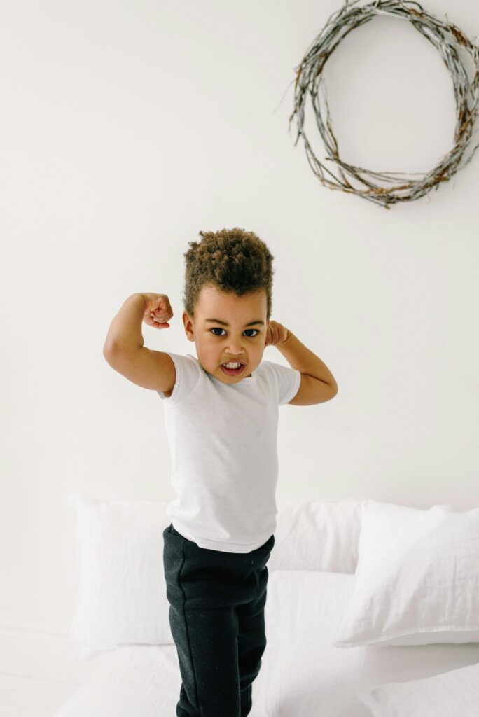 Charming young boy striking a playful flexing pose in a comfortable home environment.