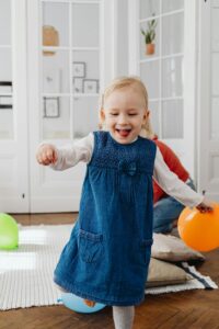Happy toddler in a blue dress playing with colorful balloons indoors.